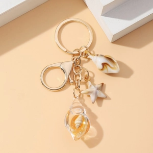 Detailed close-up of a gold metal keychain with glowing resin seashell and starfish charms
