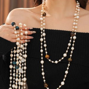 Detail of layered pearl necklace with tiger eye beads and gold clasp on black knitwear