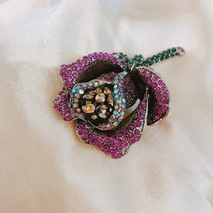 Detailed macro view of a rose brooch with vibrant magenta crystals and silver metal