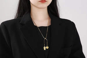 Detail of a gold snake chain necklace with a heart tag and little girl silhouette pendant