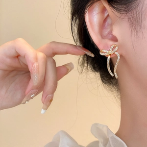 Close-up of elegant gold bow earrings with crystal accents worn by a model