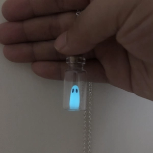 Detailed view of a glowing ghost charm inside a small glass bottle on a silver chain