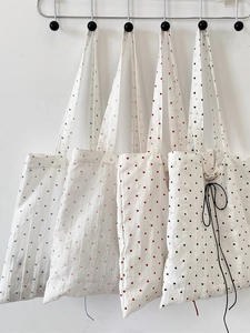 Minimalist canvas tote bags with heart patterns in four colors hung on white wall