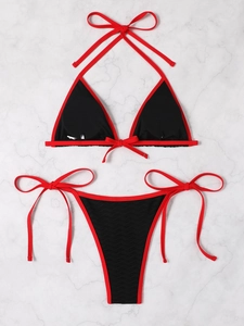 Flat lay of black ribbed bikini with red trim showing detailed fabric texture and ties