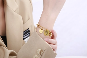 Detail of gold expandable stainless steel bracelet with heart and girl pendants on wrist