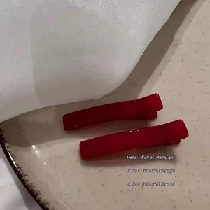 Detail view of two shiny red rectangular hair clips on a ceramic plate for girls