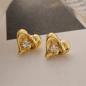 Close-up of golden heart earrings with hammer-textured metal and sparkling zircon stone