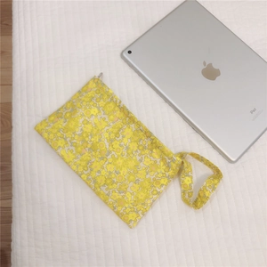 Detail of yellow floral cotton pouch with zipper and wrist strap next to iPad
