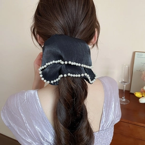 Detail of a black fabric scrunchie with pearl edge decoration worn on a ponytail