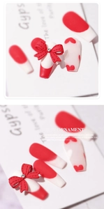 Macro detail of 3D red ribbon bow ornament and heart pattern on french tip press-on nails