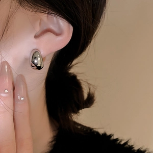 Detailed macro shot of silver bean-shaped C-style earrings with a polished mirror finish