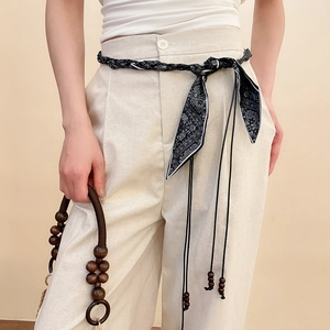 Close-up of a vintage black rope waist belt with wooden beads on cream trousers