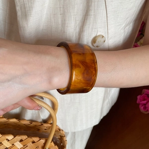 Close-up of a wide amber tortoiseshell resin bangle worn on the wrist with retro style