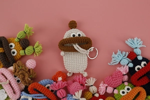 Detail of colorful handmade crochet monster key cases in beige, pink and green