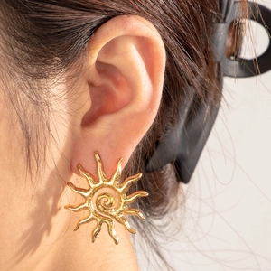 Golden sunburst stud earrings with spiral core and textured rays on model