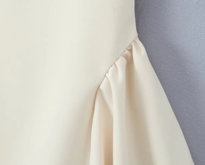 Nahaufnahme der eleganten seitlichen Raffung und Plissee-Details an einem cremefarbenen Kleid