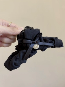 Dettaglio ravvicinato di una molletta per capelli a fiocco nero con ciondolo in metallo