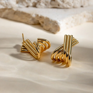 Detailed view of gold X-shaped crisscross hoop earrings on a textured stone surface