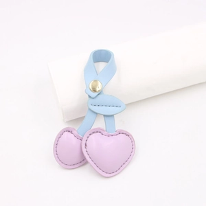 Close-up of heart-shaped leather cherry bag charm with purple fruit and blue leaves
