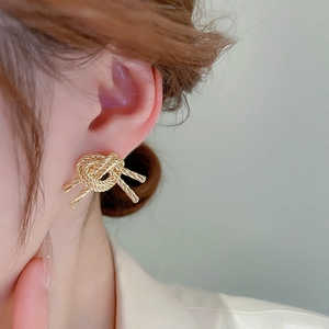 Close-up of gold metallic twisted rope knot stud earring worn on model's ear