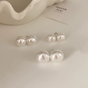 Three pairs of white pearl earrings in various sizes displayed on a ceramic tray detail