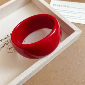 Detail of a thick red acrylic resin bangle with a glossy finish on a classic tray