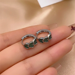 Macro shot of silver heart earrings with green zircon micro-inlay on silk fabric