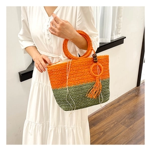 Detail of handwoven straw tote bag with orange and green dual-tone and wood bead tassel