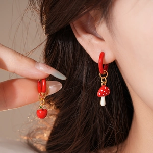 Detail of asymmetric stainless steel earrings featuring red enamel mushroom and apple charms