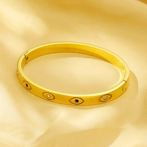 Macro shot of gold evil eye bangle with blue rhinestones on champagne silk fabric