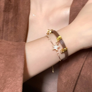 Close-up of layered brown leather and gold chain bracelets with star charm on wrist