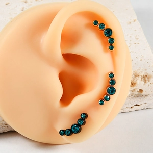 Macro detail of three-color curved stud earrings with teal stones on silicone ear model