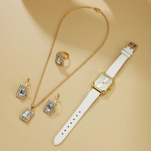 Detail of elegant gold jewelry set with rectangular gems and white leather watch
