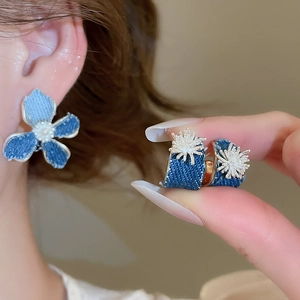 Detail view of denim fabric flower earrings with pearl accent and golden star element
