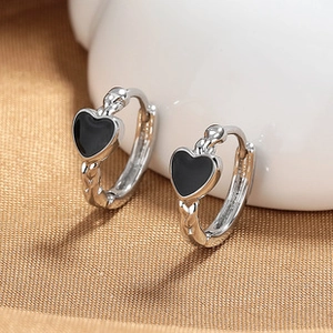 Detail of silver hoop earrings with black heart charms on a textured background