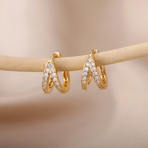 Close-up of golden C-shaped hoop earrings with sparkling zircon stones on a wood branch