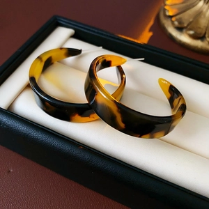 Detail of C-shaped resin earrings in tortoiseshell pattern inside a black jewelry box