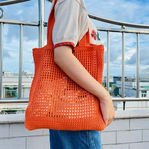 Detailed view of a bright orange hollow knit tote bag worn by a model on a sunny day