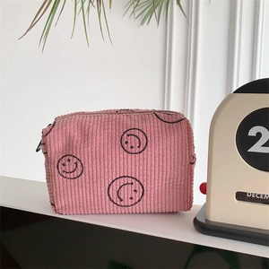 Detailed texture of pink corduroy makeup bag with a black smiley face print