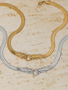 Close-up of gold and silver snake head necklaces with green eye detail on marble