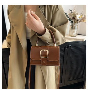 Dettaglio della borsa a tracolla marrone vintage con fibbia dorata indossata dalla modella