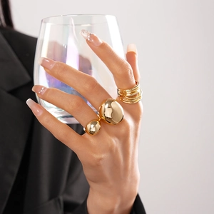 Detailed shot of gold oval bean ring and layered bands on hand with glass cup