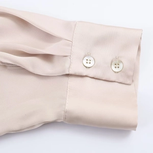 Detail of champagne satin shirt cuff featuring silk-like texture and dual white buttons