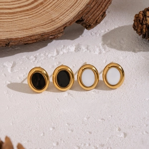 Golden geometric oval stud earrings with black and white inlays on white sand background