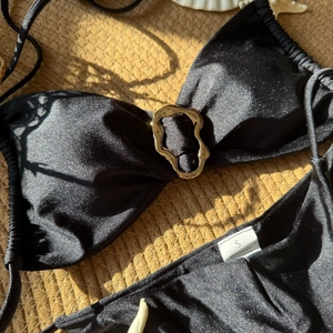 Detail eines schwarzen Bikinis mit goldener Wellenschnalle auf einer Strandstrohmatte