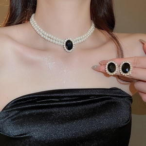 Detail view of double-layer pearl necklace and matching stud earrings with black gemstone