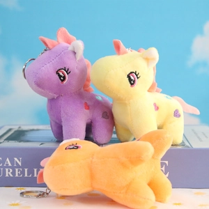 Plush unicorn horse keychains in purple, yellow and orange colors on book prop
