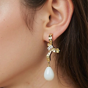 Gold bow earrings with sparkling cubic zirconia and a white teardrop pendant on a model