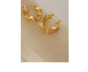 Close-up of irregular wave-textured gold plated titanium steel hoop earrings on a stand