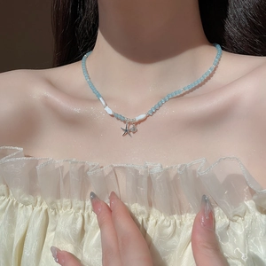 Détail de pendentifs étoile et coquillage sur un collier de perles bleues